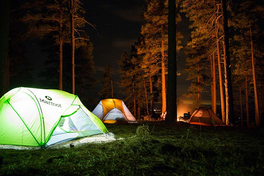 Tents lit up in the forest, with people around a campfire