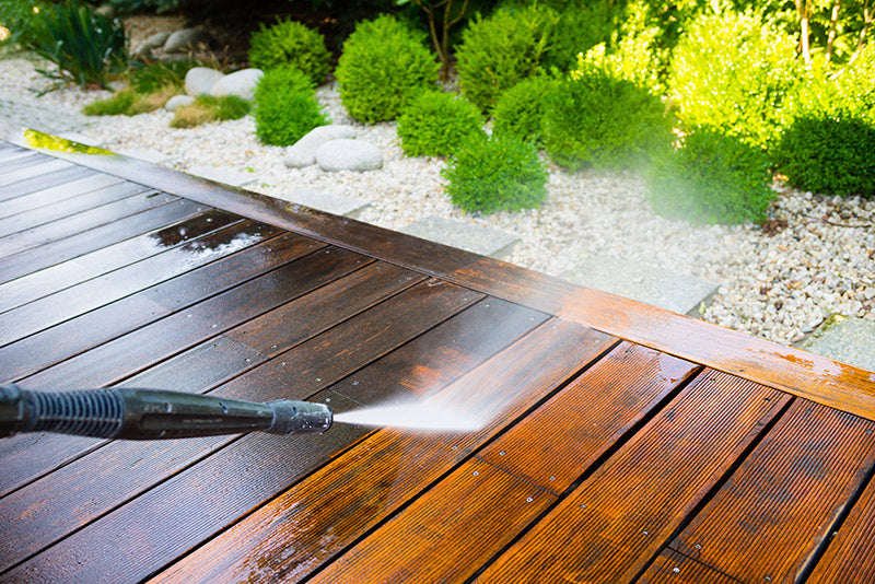 Pressure washer spraying dirt off wooden patio