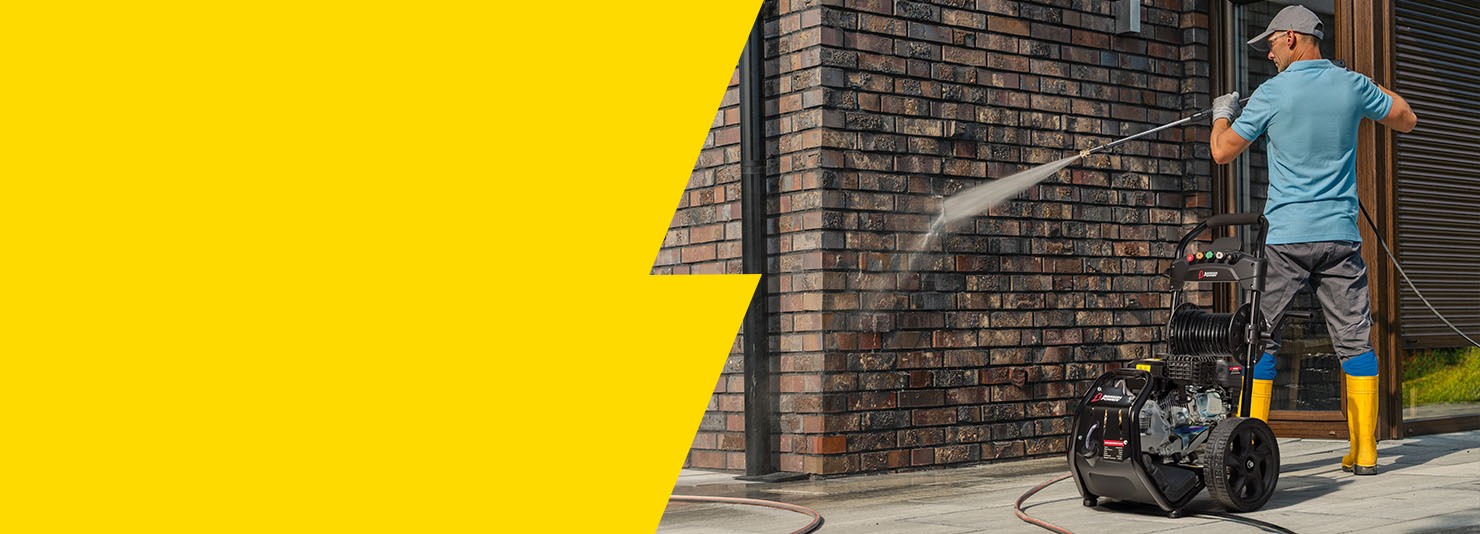 Person using a pressure washer to clean a brick wall with a yellow background