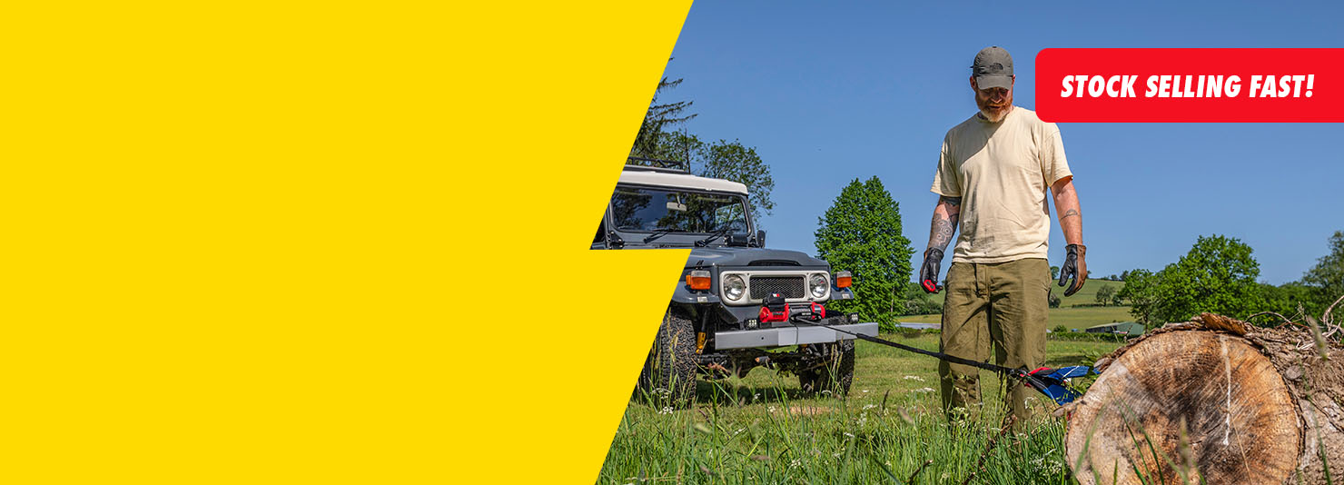 A man in outdoor work clothes stands next to a gray off-road vehicle on a grassy field, with a large yellow graphic overlay on the left and a red 'STOCK SELLING FAST!' banner in the top right.