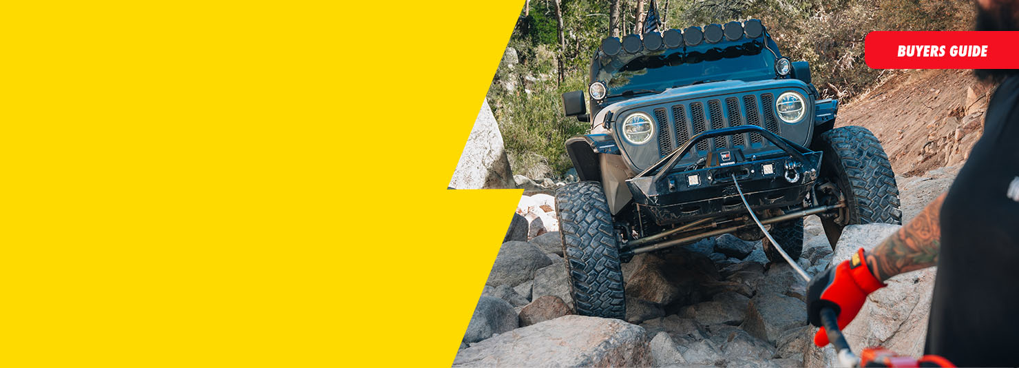 A dark blue off-road Jeep climbing rocky terrain outdoors, with part of a person in black clothing and red gloves visible on the right. A bright yellow graphic overlay dominates the left side, and a red banner in the top right reads 'BUYERS GUIDE'.