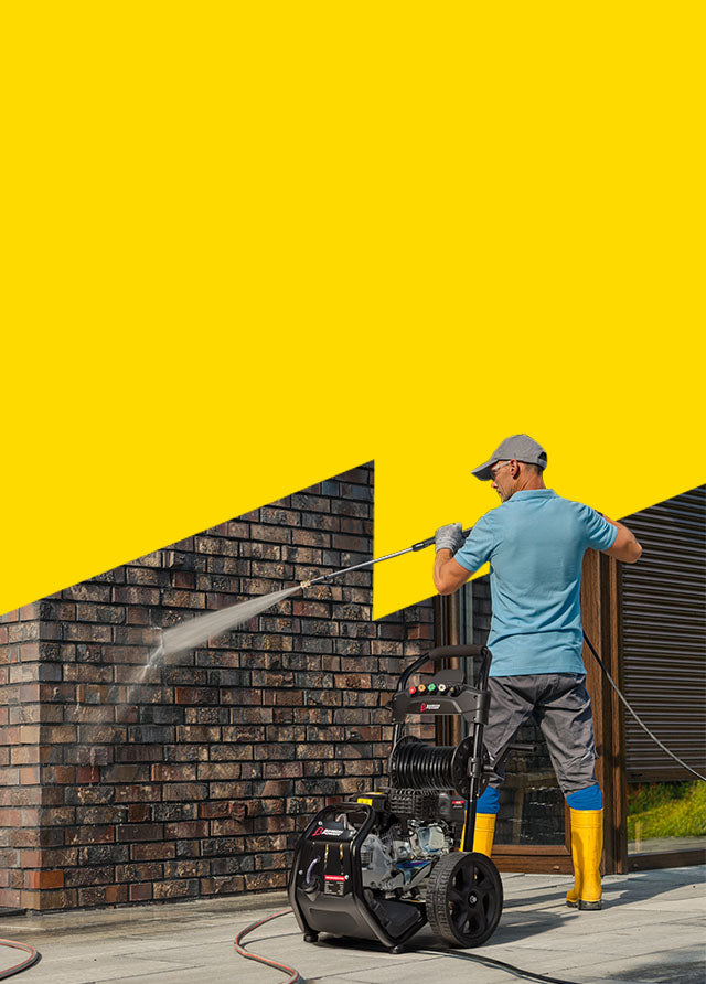 Person using a pressure washer against a yellow wall